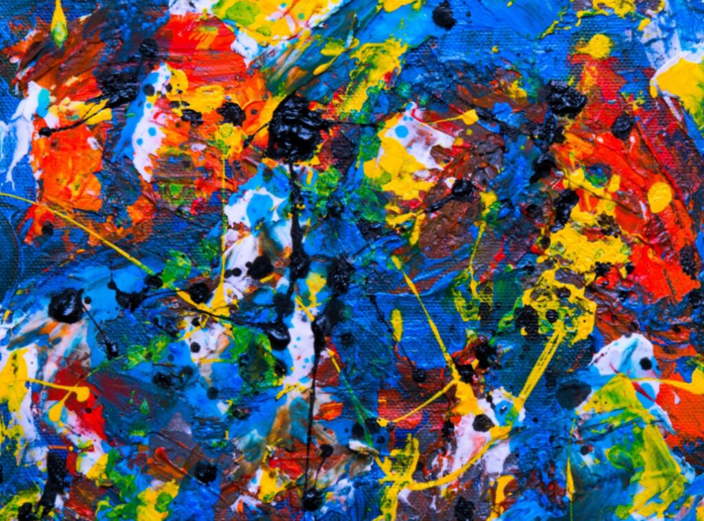 A close-up of an abstract painting: thick red, blue, yellow, and black paint splattered and layered across textured canvas.