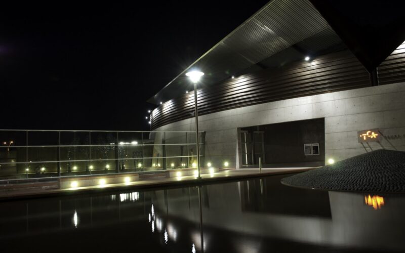 Tempe Center for the Arts at night, its angular metal roofline and lit lobby mirrored in the reflecting pool.